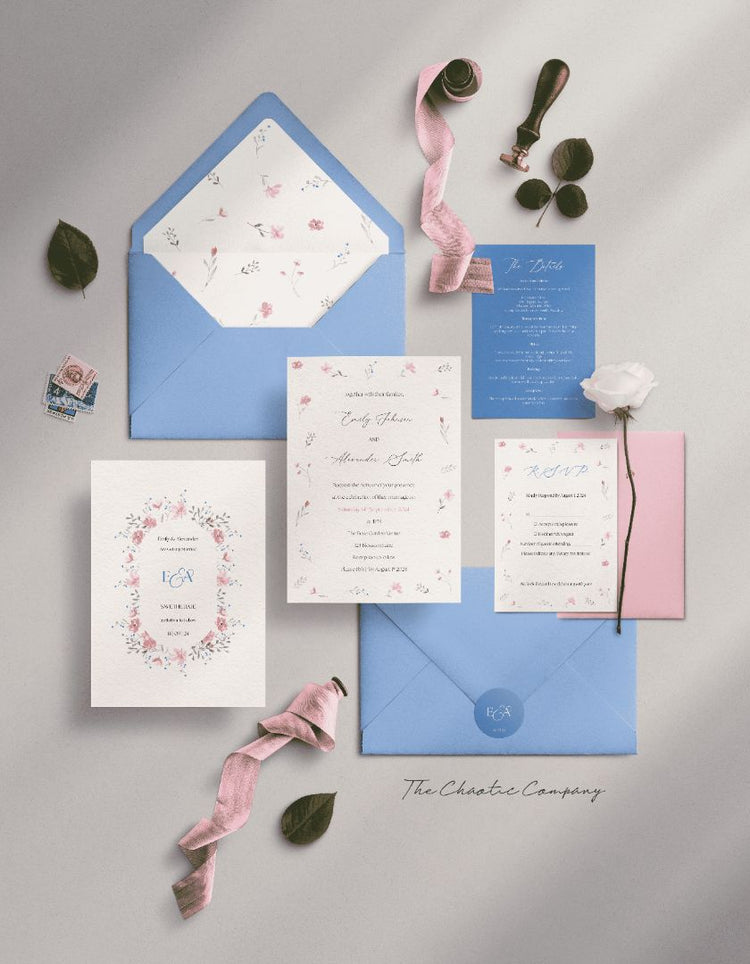 A suite with a floral theme in blue & pink tones. The suite includes a Save the Date card, an invitation card with a whimsical font, a blue details card, and a floral RSVP card, all placed in a blue envelope with a floral liner and a monogram sticker.