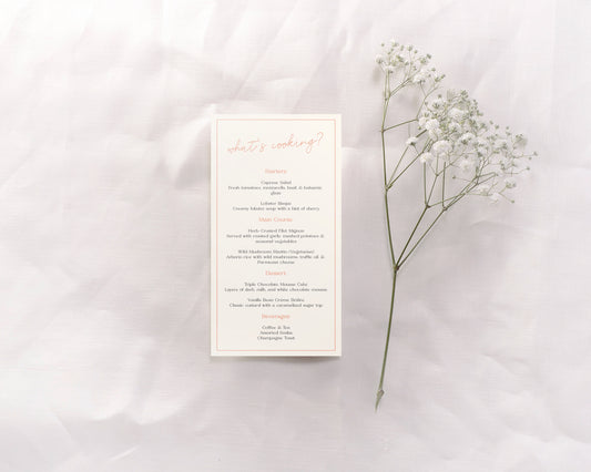 A wedding menu card featuring an understated yet chic design. The header reads "What's cooking?" in a light, elegant script at the top. The menu is divided into sections—Starters, Main Course, Dessert, and Beverages—with each section title in a soft coral color. The detailed descriptions are in a classic, minimalist black font, organized neatly and spaced for easy readability.