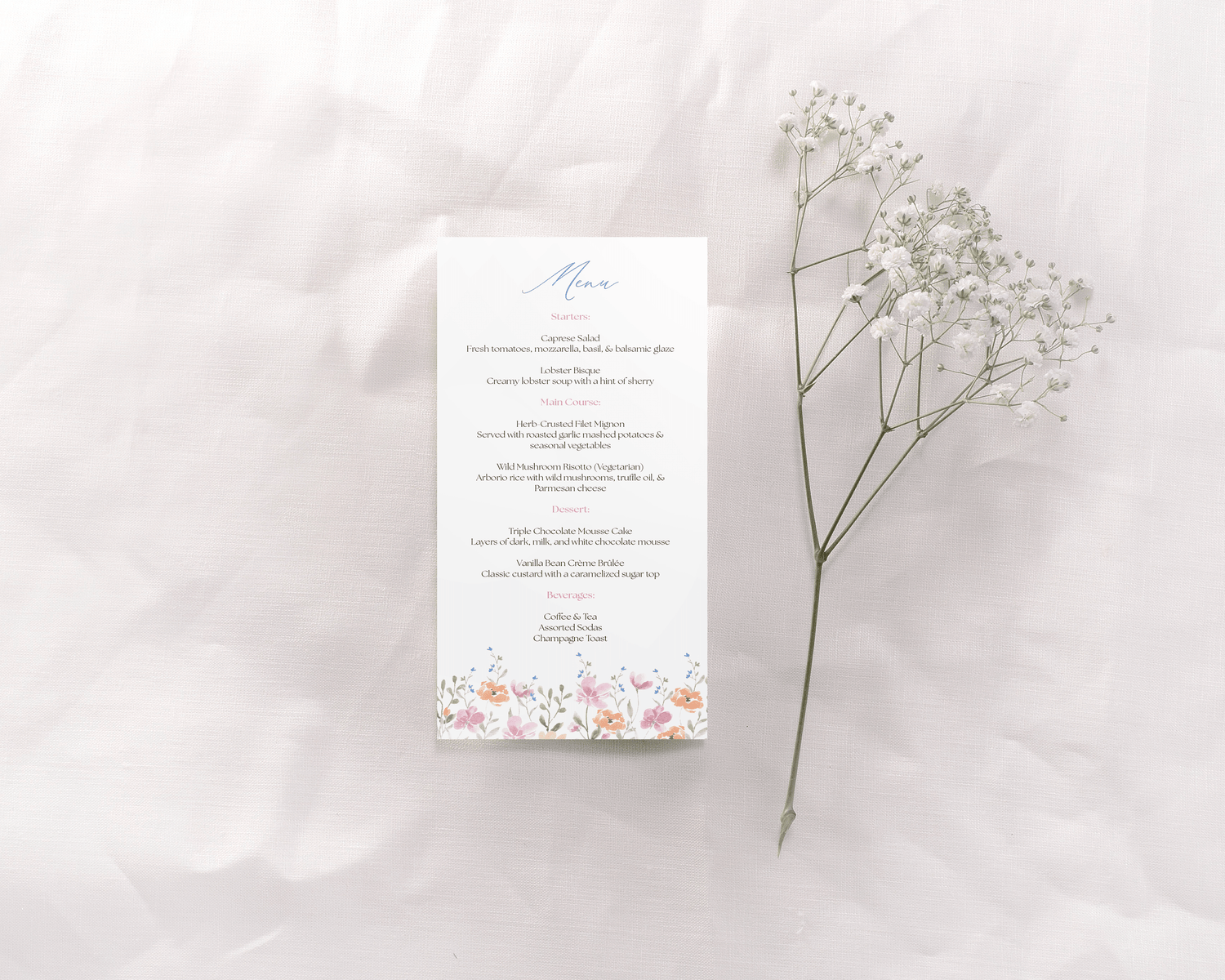 A wedding menu card featuring a floral design at the bottom, with pastel-colored flowers framing the edges. The text details the meal options. The elegant typography is accented in shades of blue and pink, matching the gentle floral theme.