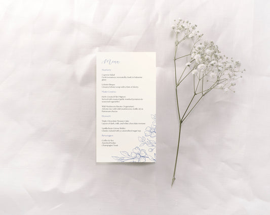 The menu card features a clean, minimalist design with elegant blue script for the "Menu" heading at the top, and the text of the menu is neatly aligned down the center of the card. The menu includes sections for starters, main course, dessert, and beverages. A simple floral illustration in blue is present in the bottom right corner of the card, adding a subtle decorative touch.