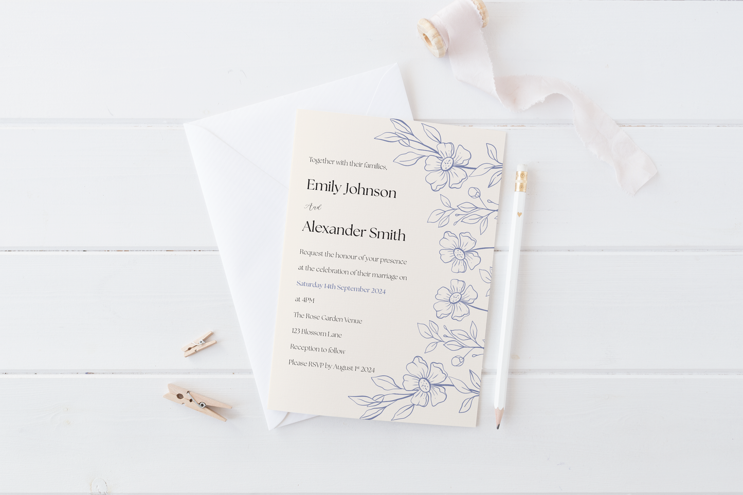 A wedding invitation laid on a white wooden surface alongside a white envelope, pencil, and decorative ribbon. The invitation includes delicate blue floral illustrations on the right edge, with text inviting guests to the wedding of Emily Johnson and Alexander Smith on 14th September 2024 at The Rose Garden Venue, followed by reception details.