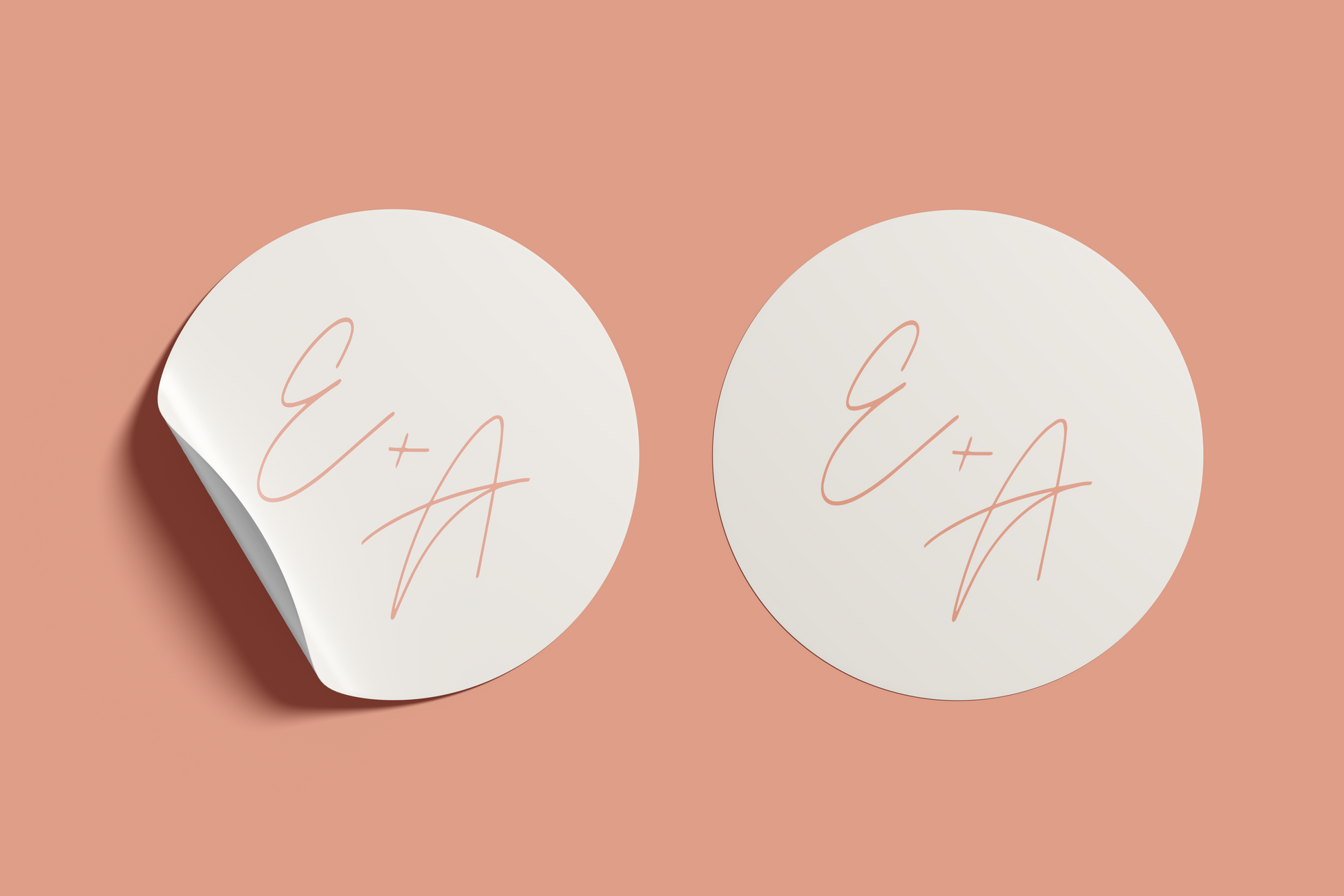 Two versions of a circular wedding sticker featuring the initials "E + A" in a peach-colored script on a cream background, with one sticker peeling slightly at the edge, all set against a muted peach backdrop.