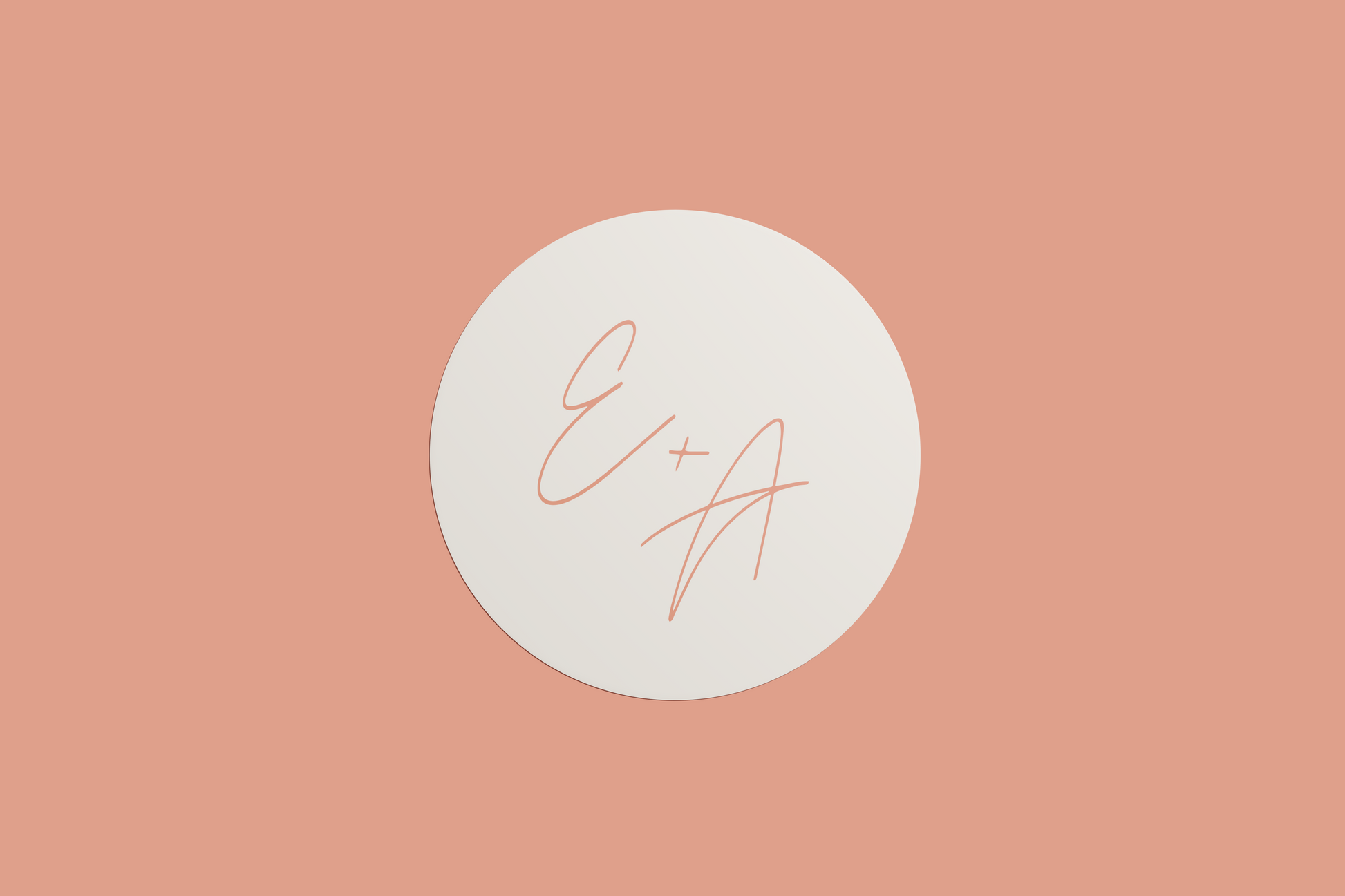 A circular wedding sticker with the initials "E + A" written in a simple, thin script in a peach tone, set against a cream background, all placed on a muted peach-coloured background.