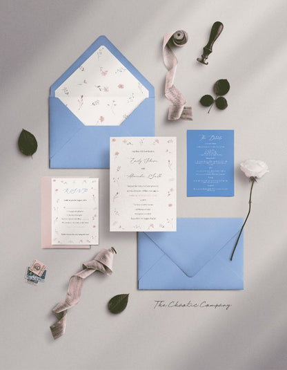 A wedding invitation suite in soft floral designs with light blue and blush tones. The suite includes an invitation card featuring the names "Emily Johnson and Alexander Smith" framed by delicate floral accents, a matching RSVP card in pink, a blue details card, and a coordinating blue envelope with a floral-patterned liner.