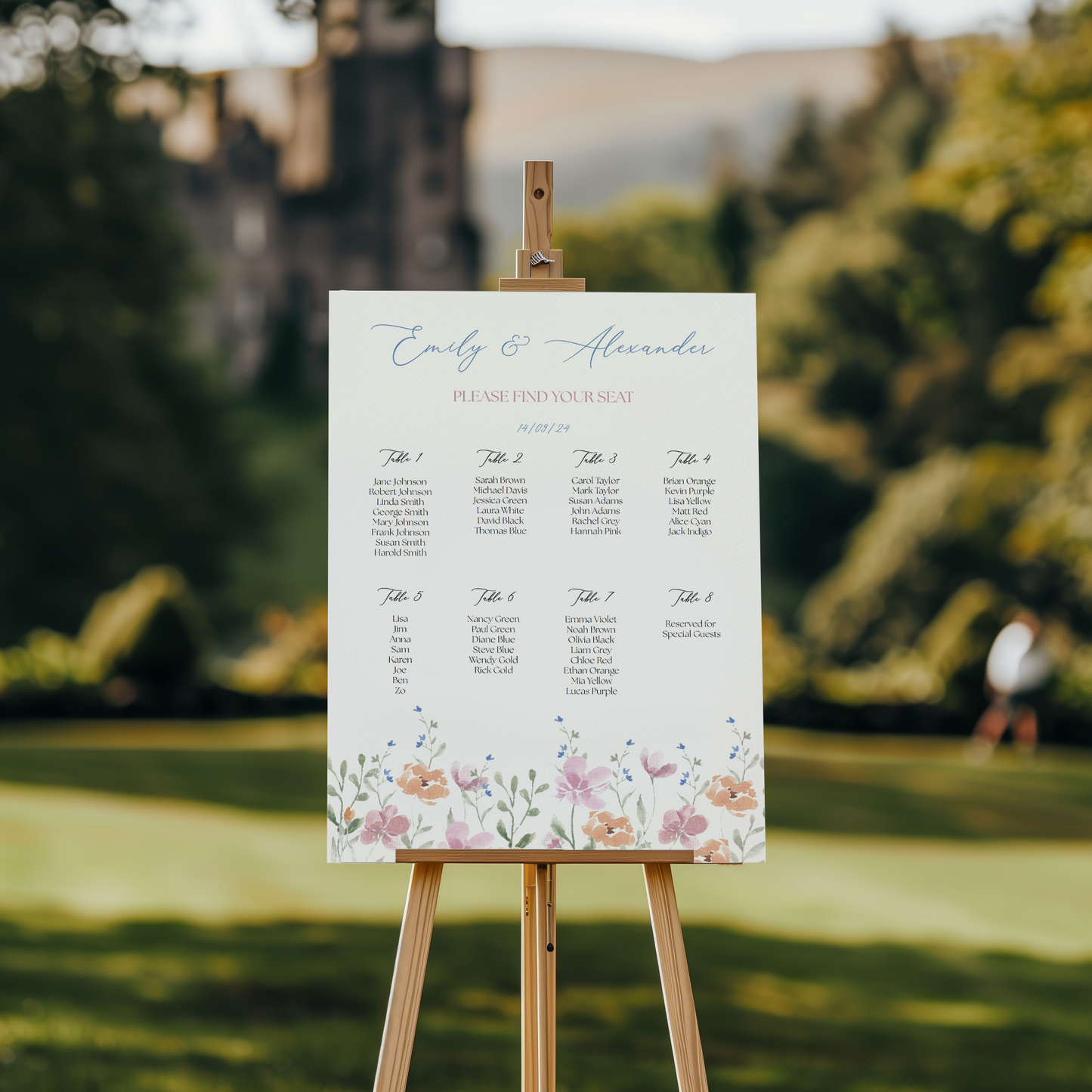 A wedding seating chart on an easel in a garden, with a castle blurred in the background. Titled "Emily & Alexander" in blue script, it lists eight tables with guest names and the date "14/09/24." A floral border with pastel flowers decorates the bottom, adding a romantic touch to the elegant outdoor setting.