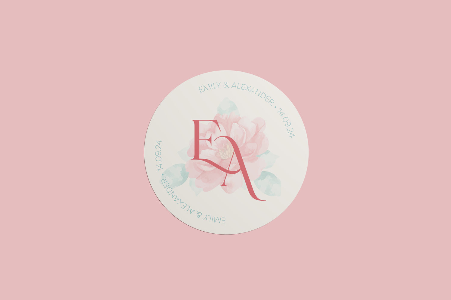 A circular wedding sticker featuring the initials "E & A" in a bold pink serif font, set against a soft watercolour floral background. The names "Emily & Alexander" and the date "14.09.24" are written around the border in a light teal serif font, all placed on a light cream background against a soft pink backdrop.