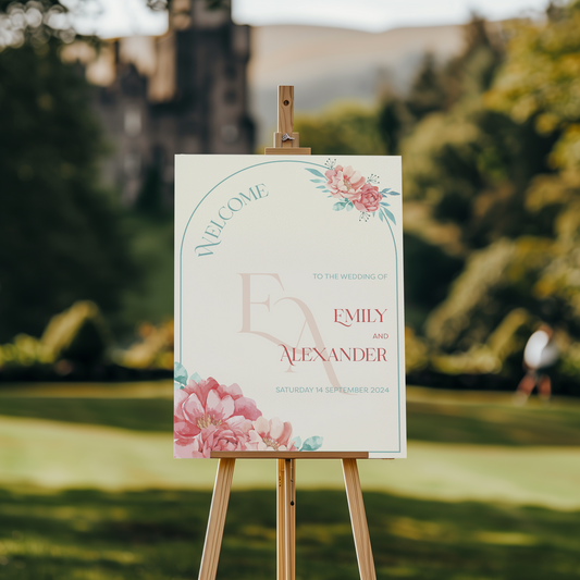 A welcome sign featuring floral accents in pink and green, framing the words "Welcome to the wedding of Emily and Alexander." The couple's initials "E & A" are prominently displayed in a large, elegant font, while the date "Saturday 14 September 2024" is written below.